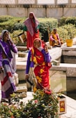 woman in purple and red sari standing beside woman in purple and white hijab