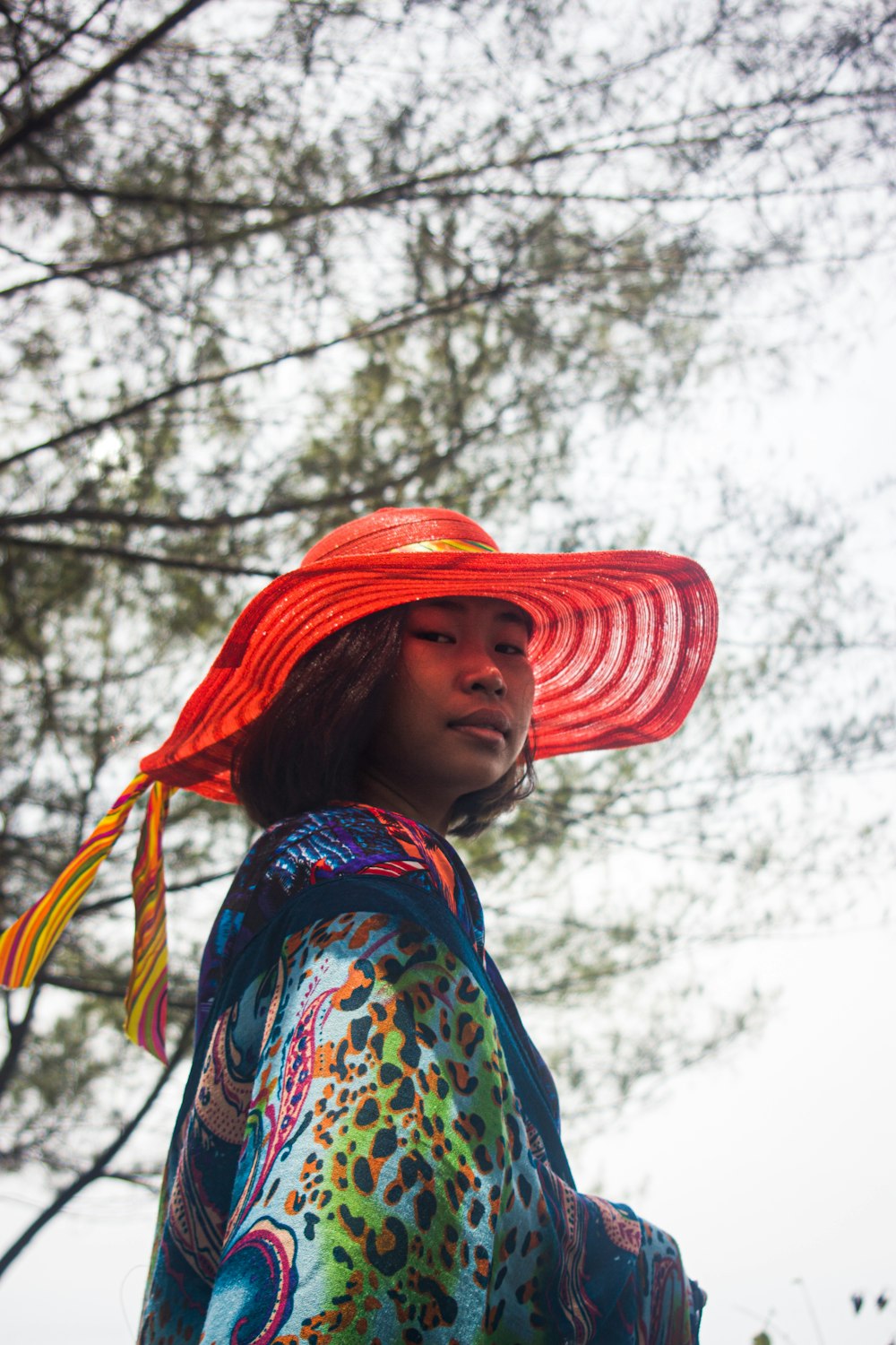 woman in blue and red floral scarf and brown hat standing near bare trees during daytime