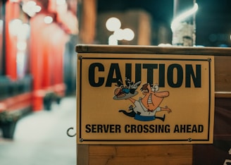 A yellow caution sign warns of a server crossing ahead, featuring a cartoon character of a person balancing a tray with a drink.