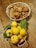 On a rustic wooden table, a woven basket is filled with wild mushrooms exhibiting shades of brown and orange. A second basket contains several bright yellow quinces, some with green leaves attached, providing a fresh and natural look.