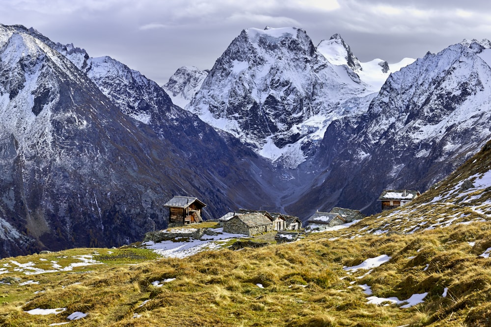 Braunes Holzhaus auf grünem Grasfeld in der Nähe eines schneebedeckten Berges tagsüber