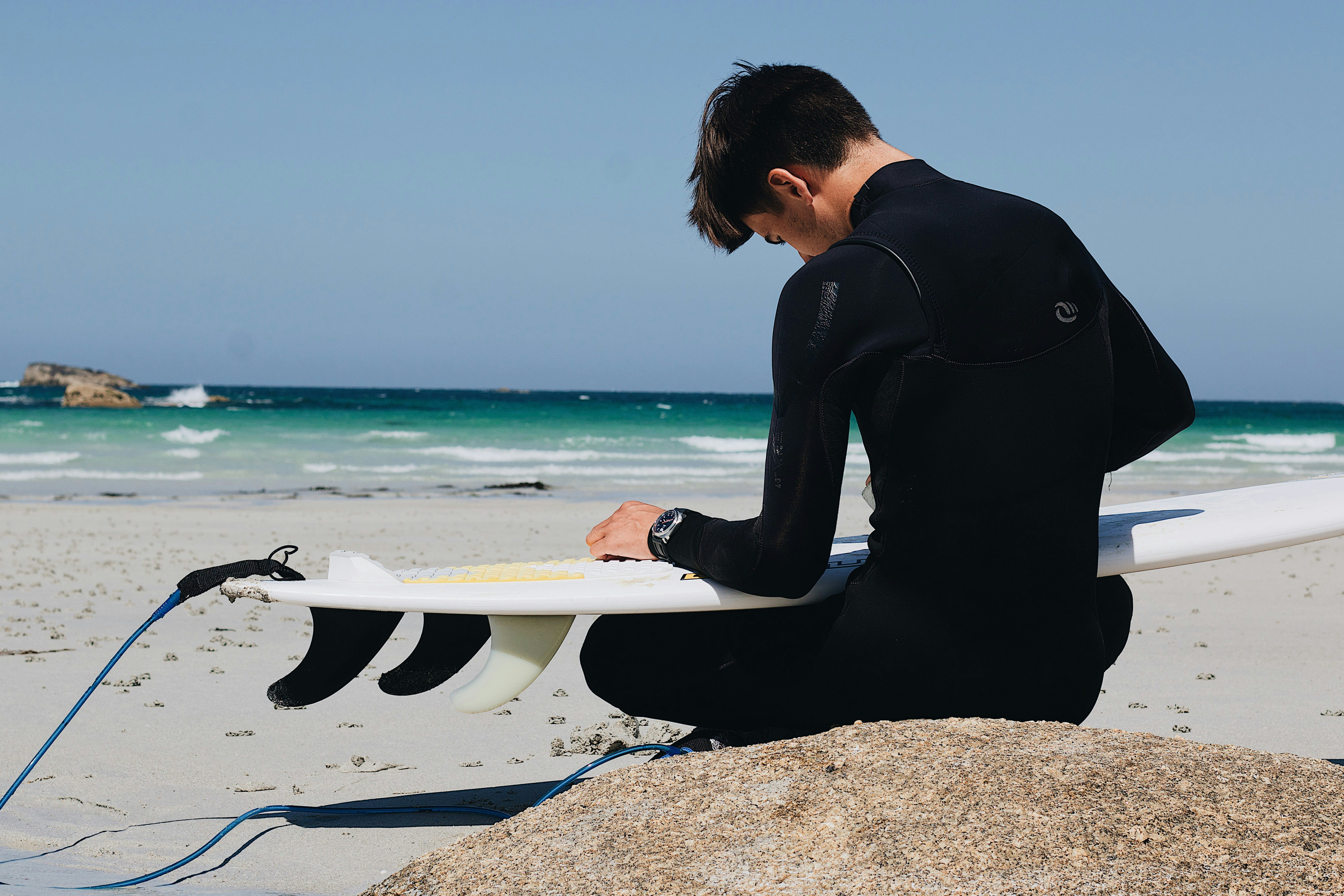 man in black long sleeve shirt sitting on white surfboard on beach during daytime