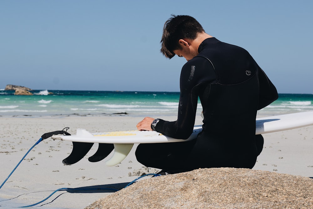 man in black long sleeve shirt sitting on white surfboard on beach during daytime