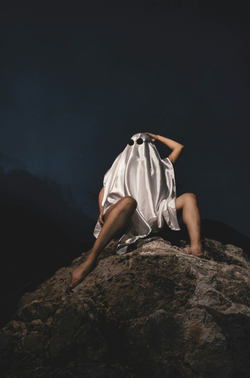 woman in white dress sitting on brown rock