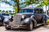 A tow truck loading an old rusty car in a Coral Gables driveway under bright sunlight.