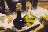 A wooden table displaying several bottles of agretta vinagres with natural herbs and flowers around.