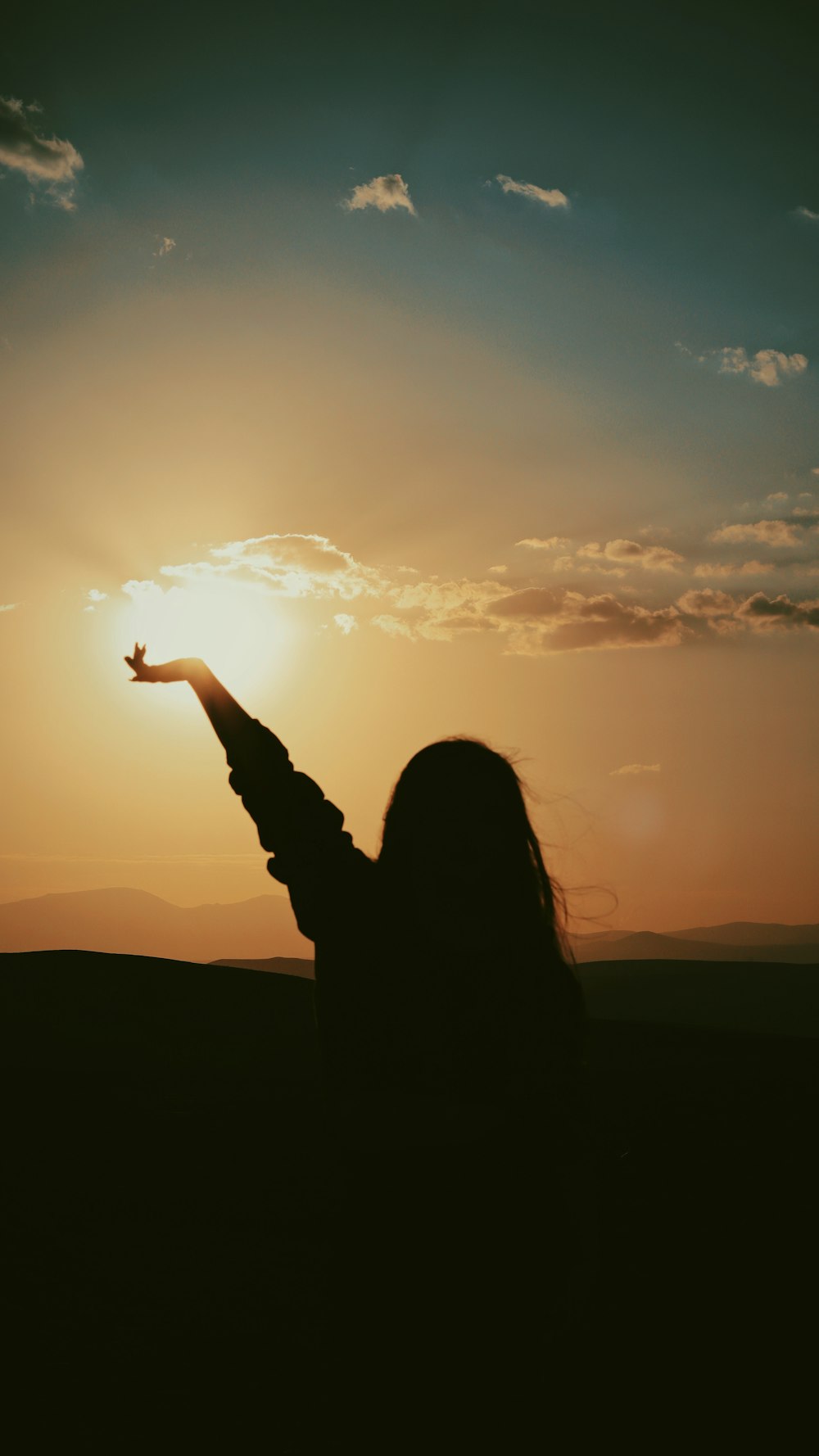 silhouette of woman raising her hand during sunset