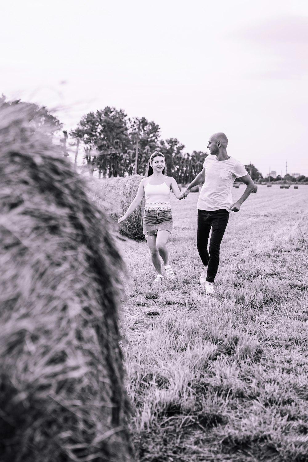 grayscale photo of man and woman walking on grass field