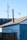 A wooden fence stands in front of an old building with a sloped roof. A tall metal chimney rises from the roof. Visible are electrical wires and a light pole in the background against a clear blue sky.