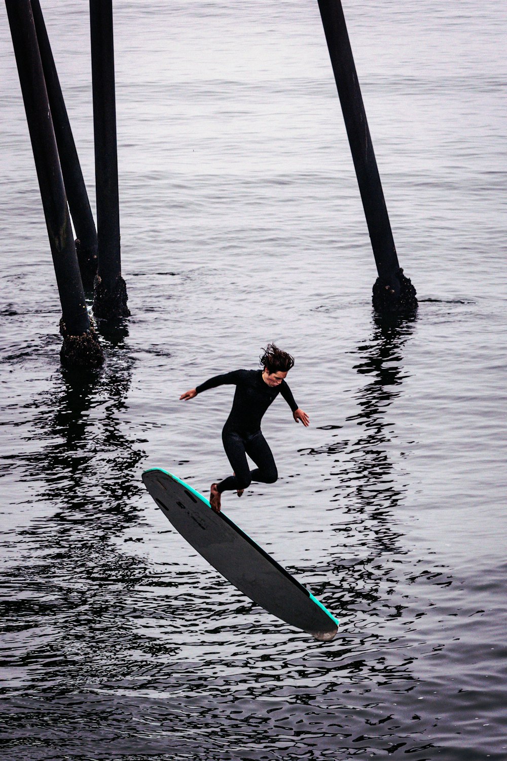 낮 동안 물에 서핑 보드를 타는 검은 잠수복을 입은 여자