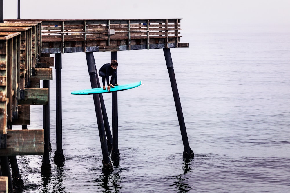 Persona in muta umida nera che tiene la tavola da surf blu sul mare durante il giorno