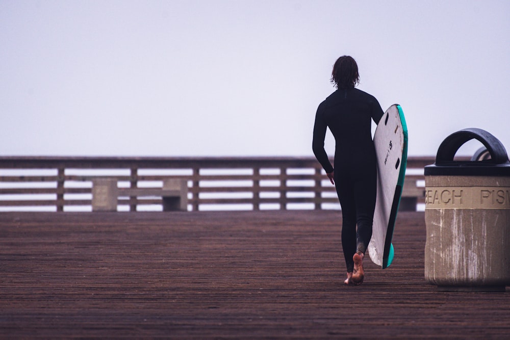 man in black tank top and black pants holding blue and white surfboard