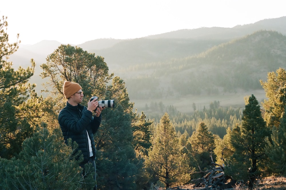 homme en veste noire prenant des photos d’arbres verts pendant la journée