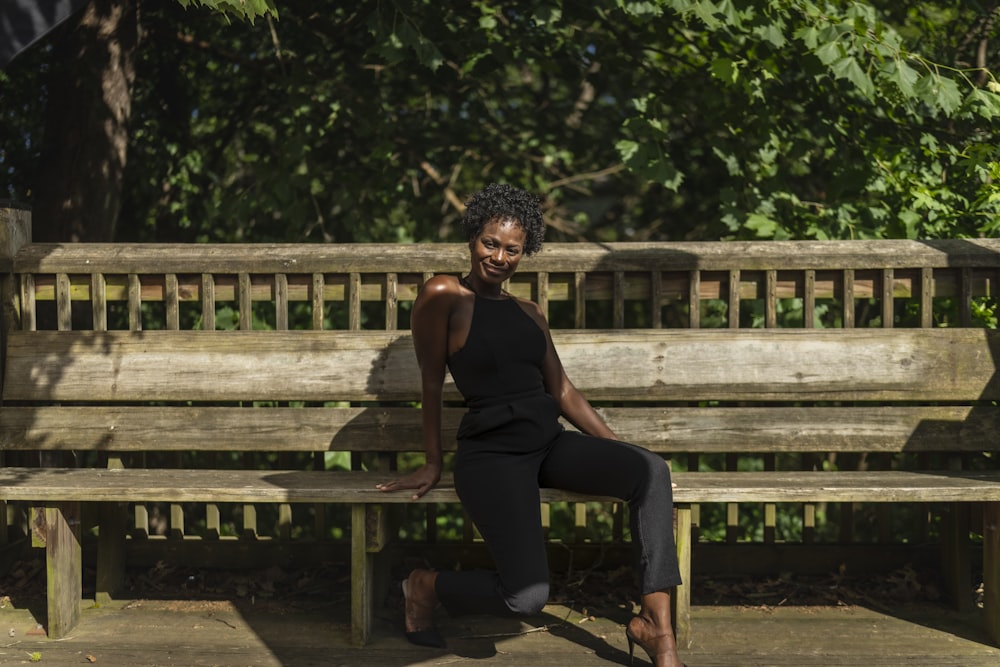 woman in black tank top and black pants sitting on brown wooden bench during daytime