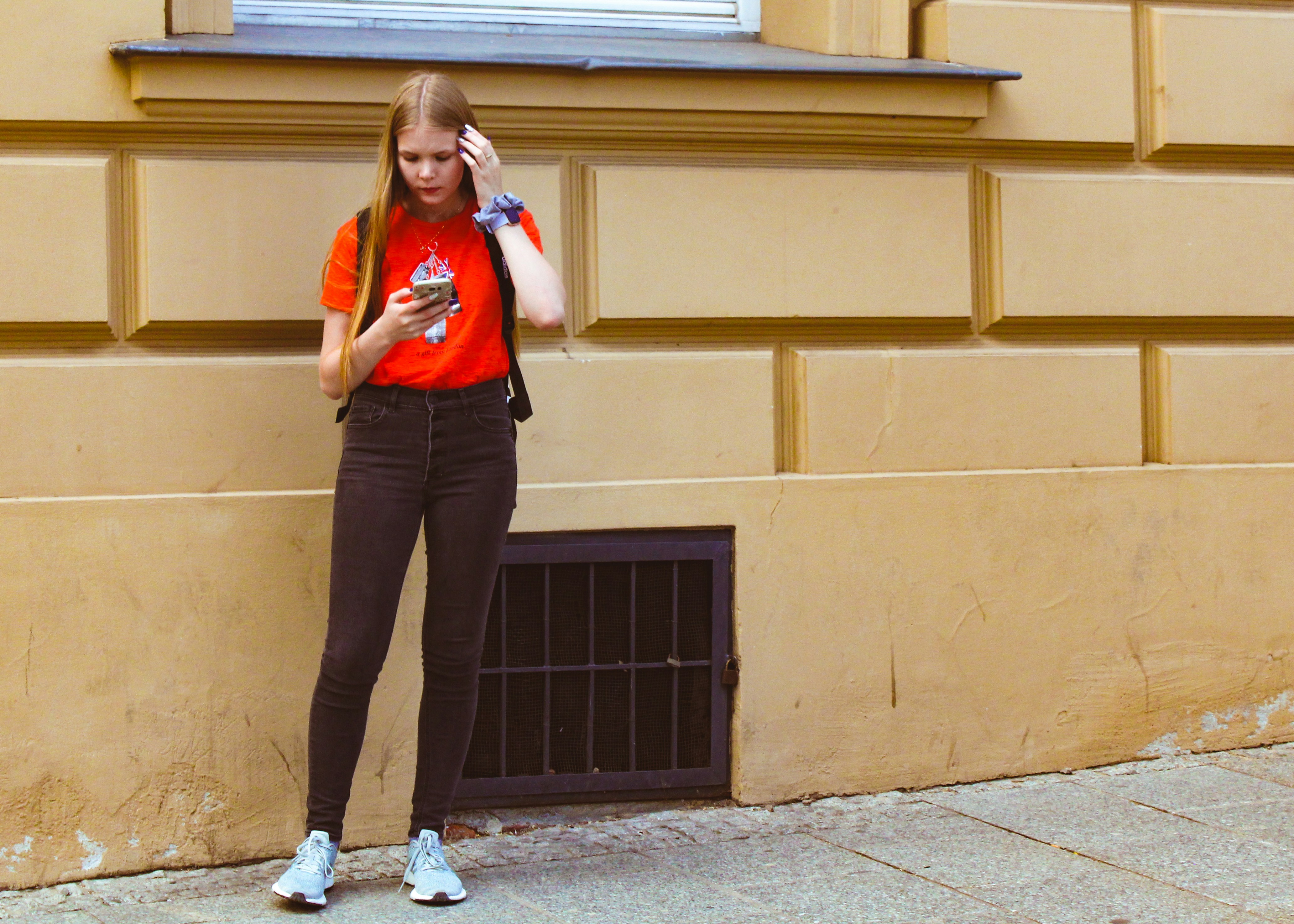 Donna in sciarpa rossa e pantaloni neri in piedi accanto all'edificio di cemento marrone durante il giorno