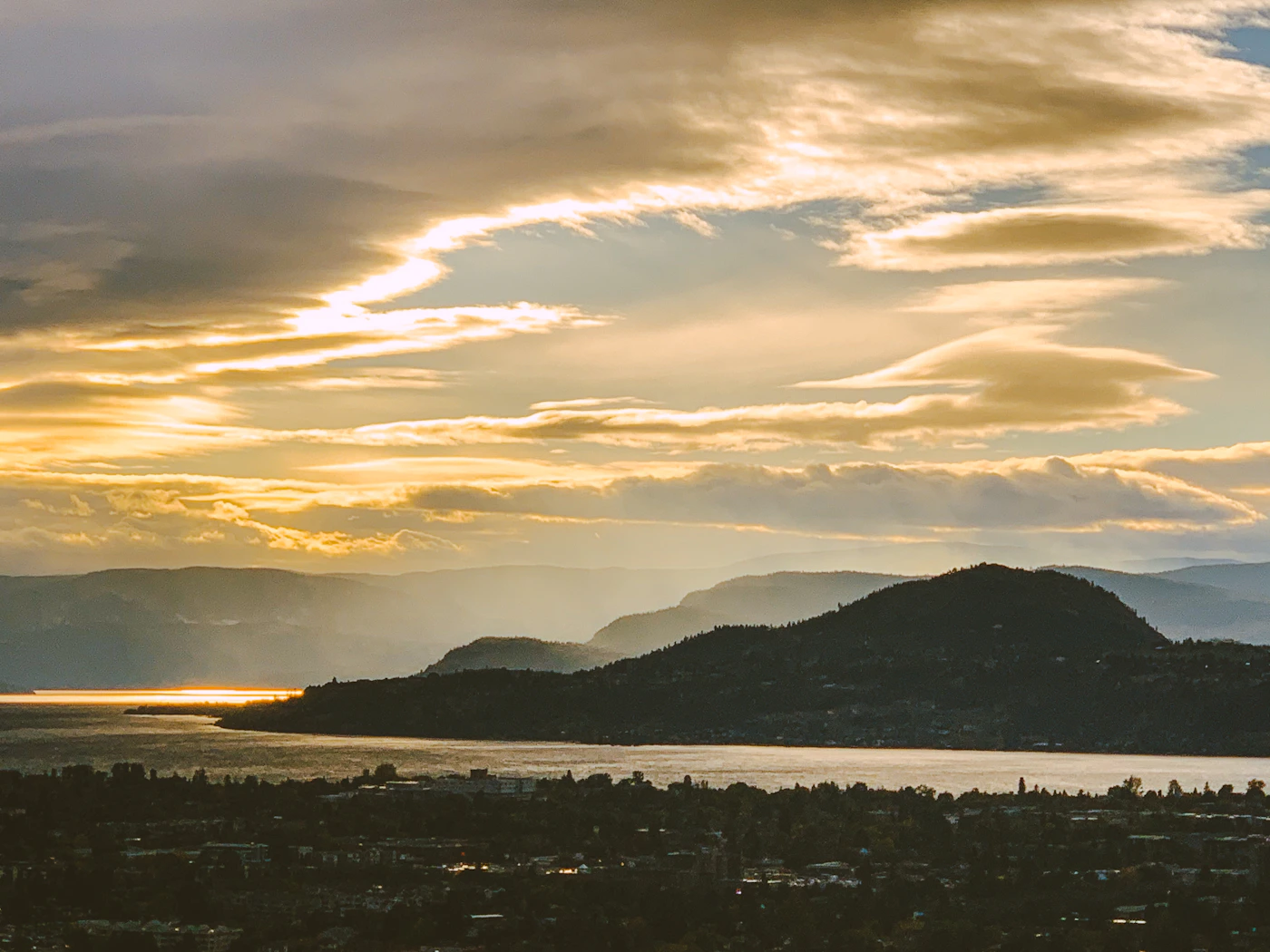 Silhouette of a Kelowna mountain at sunset with warm orange and gold sky behind it