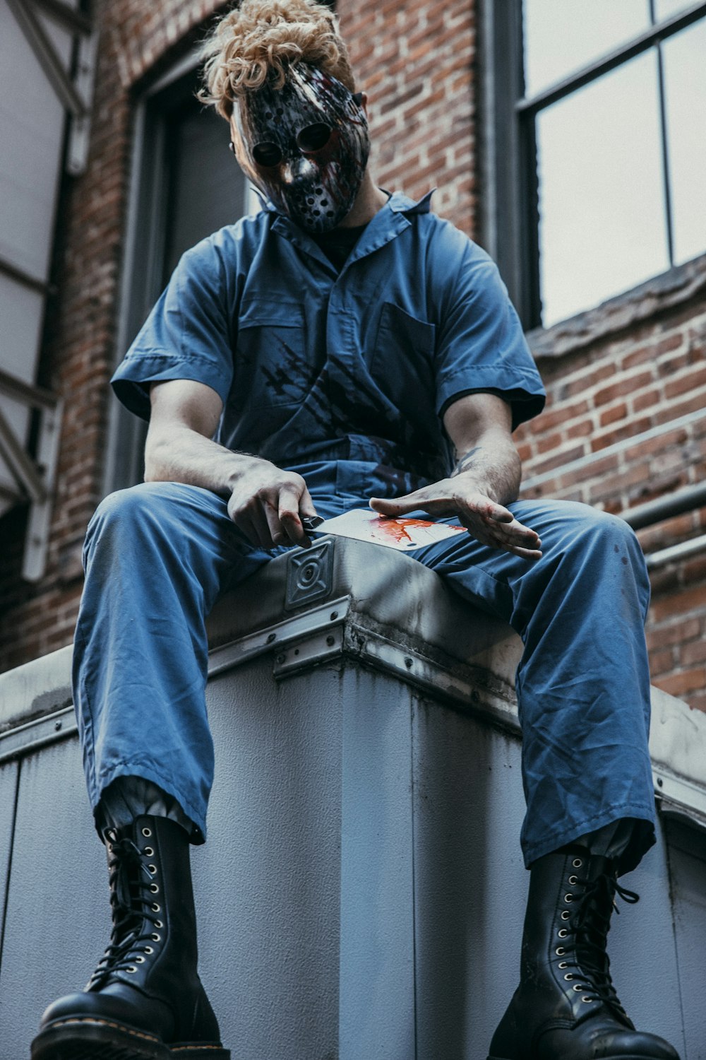 man in blue polo shirt and blue denim jeans sitting on gray concrete wall during daytime