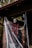 A Halloween decoration featuring a creepy clown mask with a sinister smile is hanging from the porch of a house. The red and black tattered cloth drapes around it, accented by white spider webs that are spread across the brick pillars.