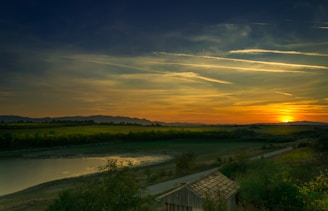 green grass field near body of water during sunset