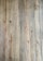 A close-up view of wooden floorboards with a natural, rustic appearance. Each plank has unique grain patterns and knots, with variations in color and texture that add character.