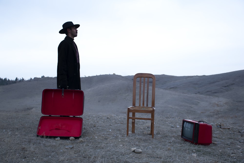 man in black jacket and black hat standing near red chair