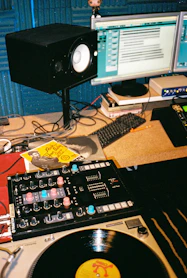 A cozy studio setup with vinyl records, mixing equipment, and a laptop displaying music software.