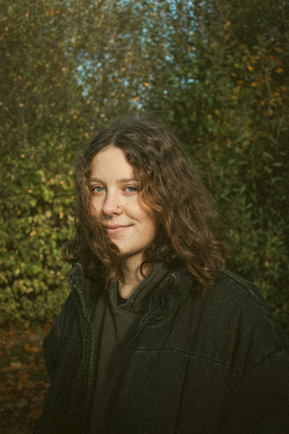 woman in black jacket standing near green trees during daytime