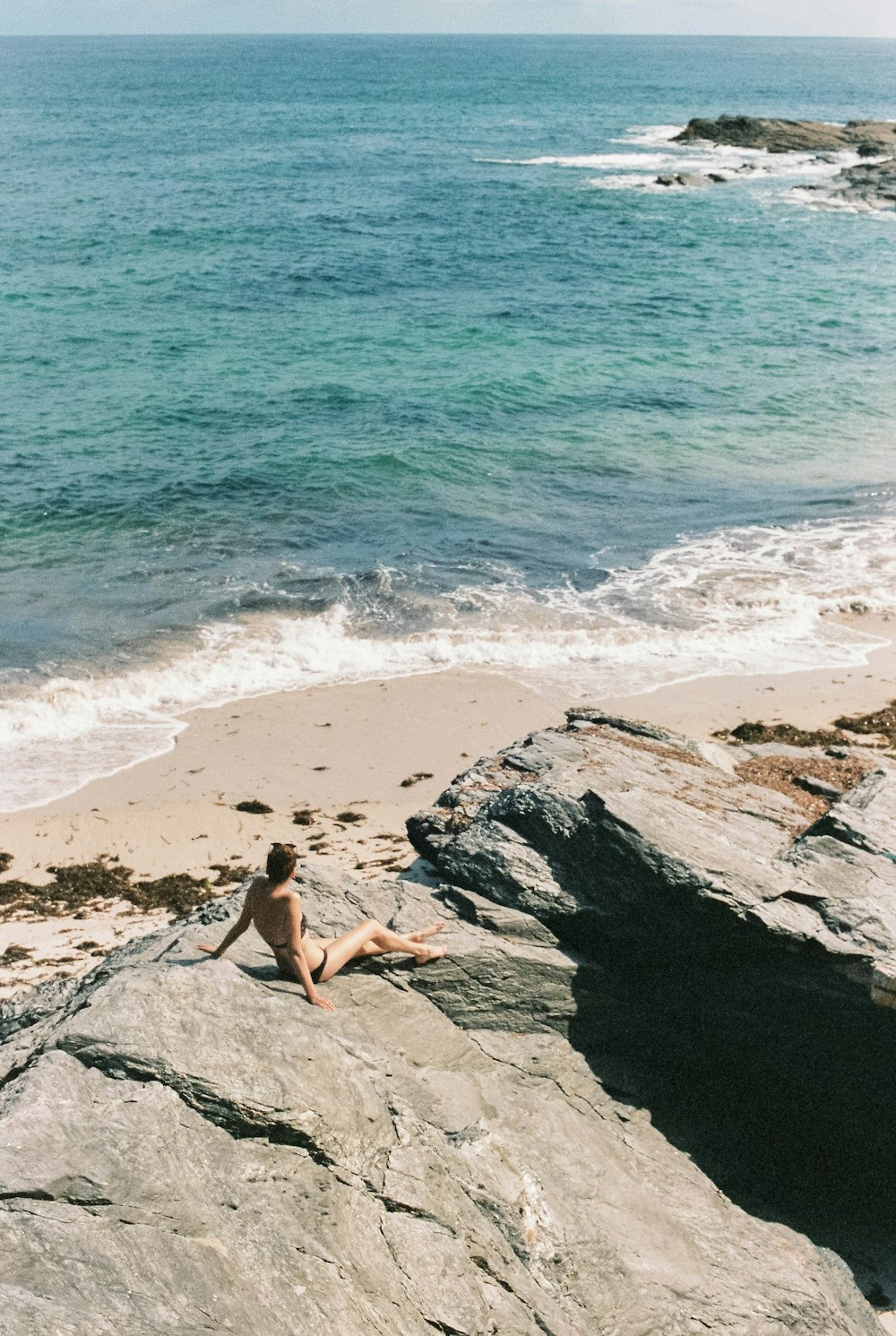 woman in white bikini lying on gray rock near body of water during daytime