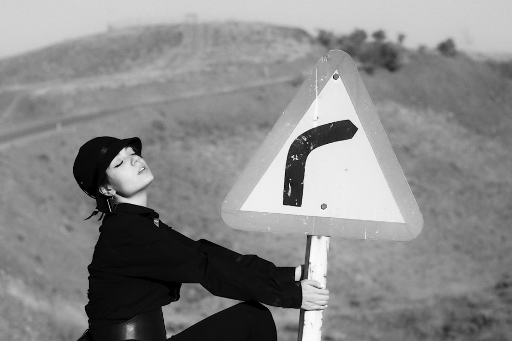 Photo en niveaux de gris d’une femme en sweat à capuche noir et pantalon noir assise sur une route blanche et noire