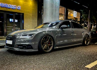 A sleek sedan with dark window tinting parked on a city street at dusk, reflecting ambient lights.