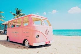 a pink vw bus parked on top of a sandy beach