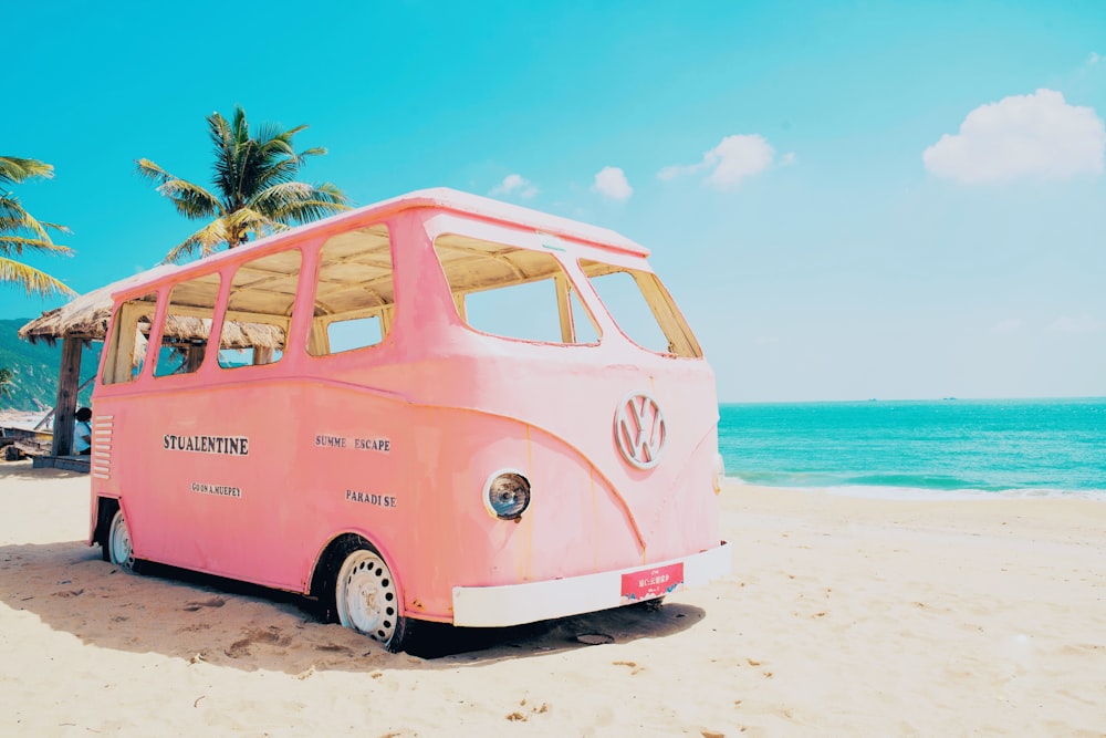 a pink vw bus parked on top of a sandy beach