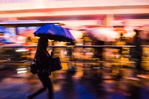 Street photography shot of a rainy city street with reflections and blurred motion of pedestrians.
