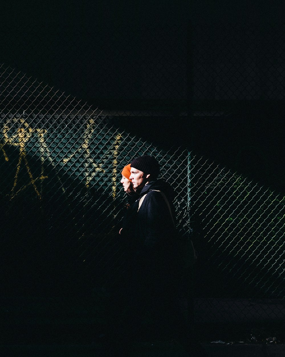 man in black leather jacket standing beside metal fence