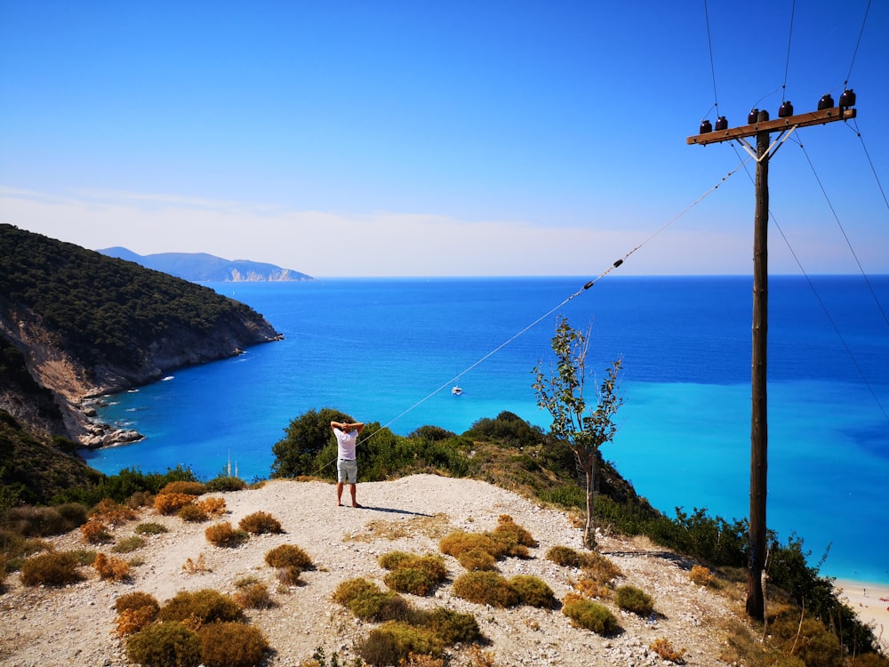 woman in white dress standing on brown rock near blue sea during daytime