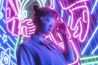 A person wearing futuristic glasses stands in front of vibrant neon lights. The background features bold electric purple, blue, and pink colors with abstract designs, possibly depicting elements like rockets or space themes. The individual is dressed in a casual outfit with a shirt and sweater, and their expression appears contemplative.