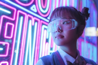 A person with their hair in a bun is wearing reflective, futuristic eyewear. The background is a neon-lit urban setting with vivid pink and blue lights. The lights create a vibrant and dynamic atmosphere, with reflections casting colorful patterns on the eyewear.