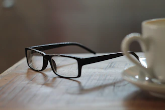 Close-up of a stylish glasses case placed next to a steaming cup of coffee.