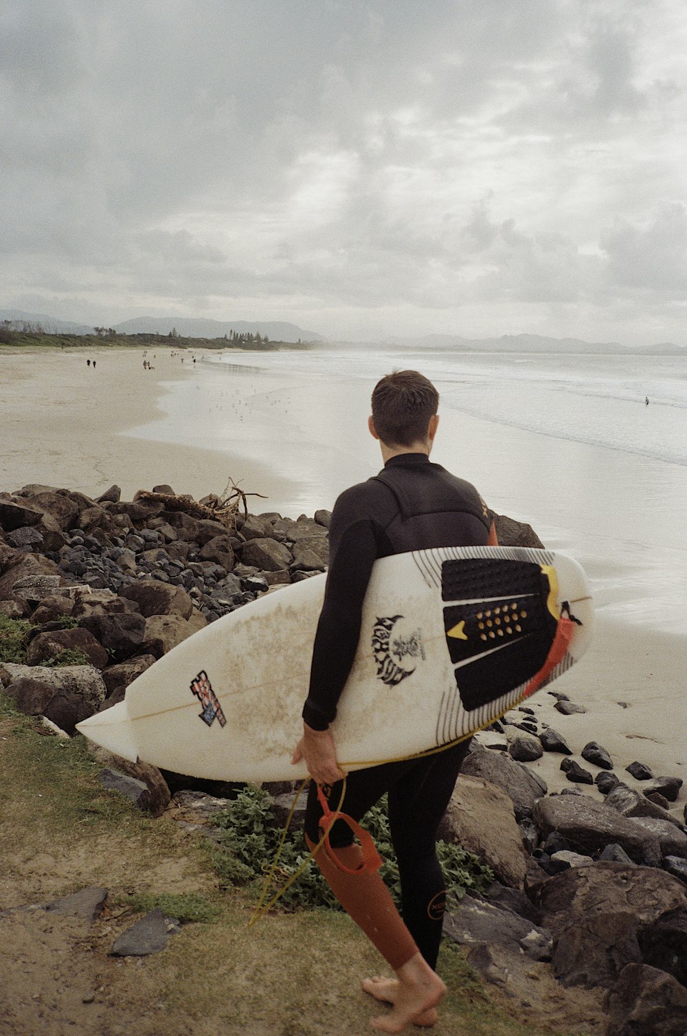 man in black jacket holding white surfboard standing on rocky shore during daytime