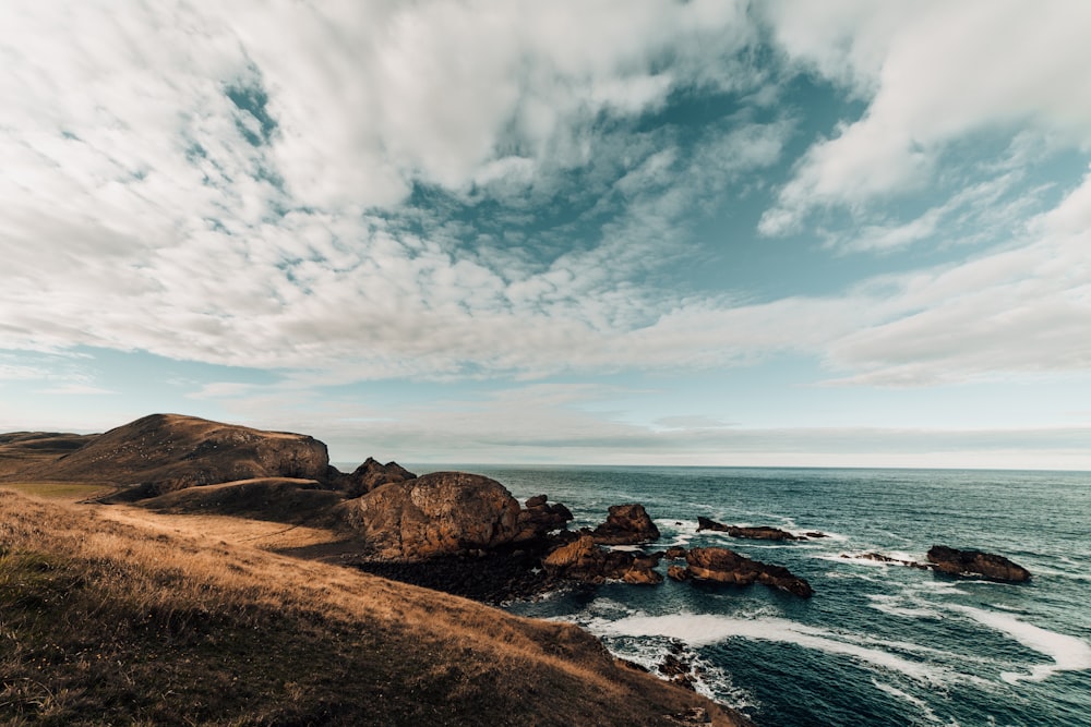 brown rock formation beside body of water under white clouds and blue sky during daytime