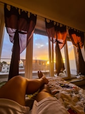 Elegant bedroom with large windows overlooking the river and hills at sunset.