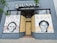 The storefront of a hair and wigs shop features two large murals with portraits of Marielle Franco and Breonna Taylor. The artwork includes text in both Portuguese and English, posing poignant questions about social justice and the impact of violence. The shop windows are boarded up, and the murals are displayed against a gray-blue exterior wall.