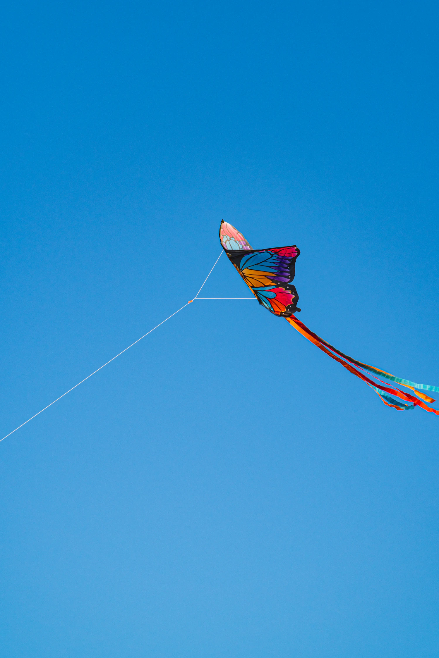 A red and yellow kite with long tails climbing into a clear blue sky