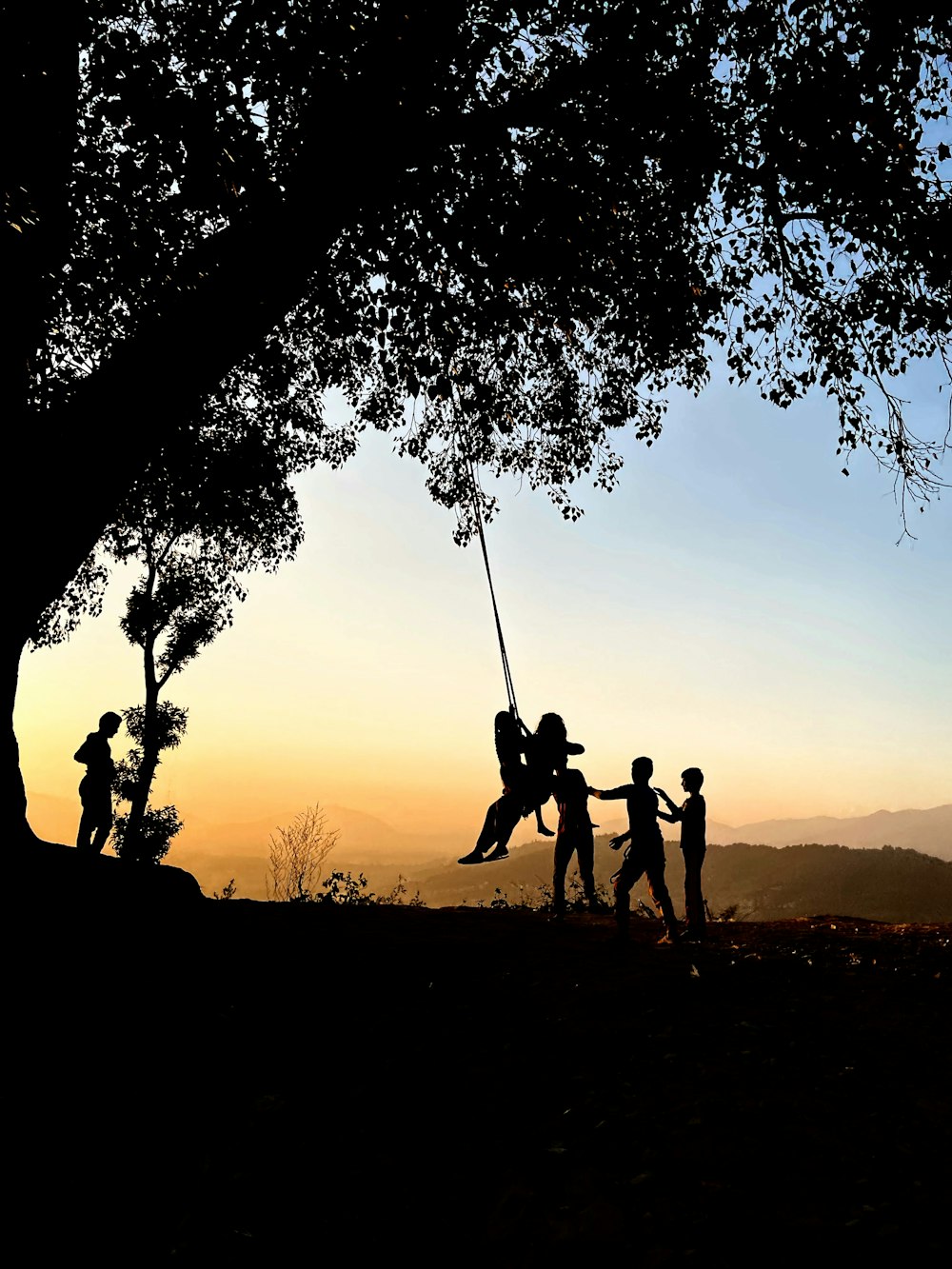 Silhouette de personnes se balançant sous un arbre au coucher du soleil