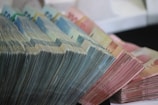 Stacks of various denominations of paper currency are neatly arranged in a cascading manner. The bills are organized in bundles, with a noticeable range of colors and sizes.