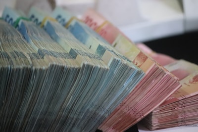 Stacks of various denominations of paper currency are neatly arranged in a cascading manner. The bills are organized in bundles, with a noticeable range of colors and sizes.