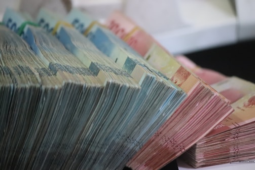 Stacks of various denominations of paper currency are neatly arranged in a cascading manner. The bills are organized in bundles, with a noticeable range of colors and sizes.