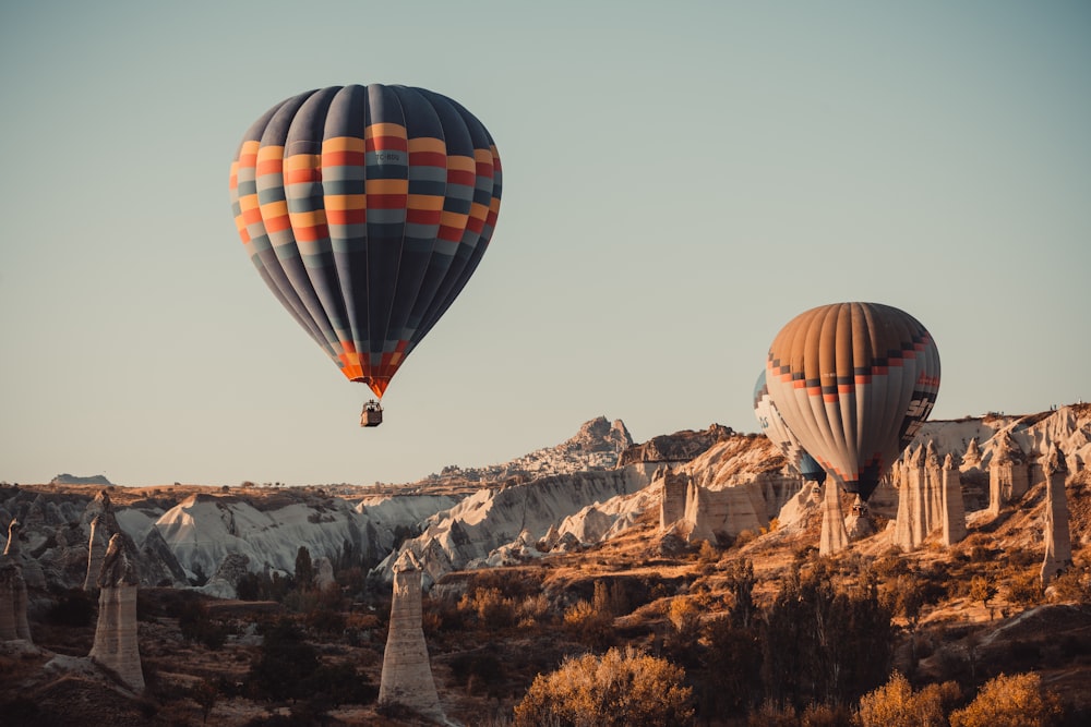 Mongolfiera rossa e nera che vola sopra la montagna rocciosa marrone durante il giorno