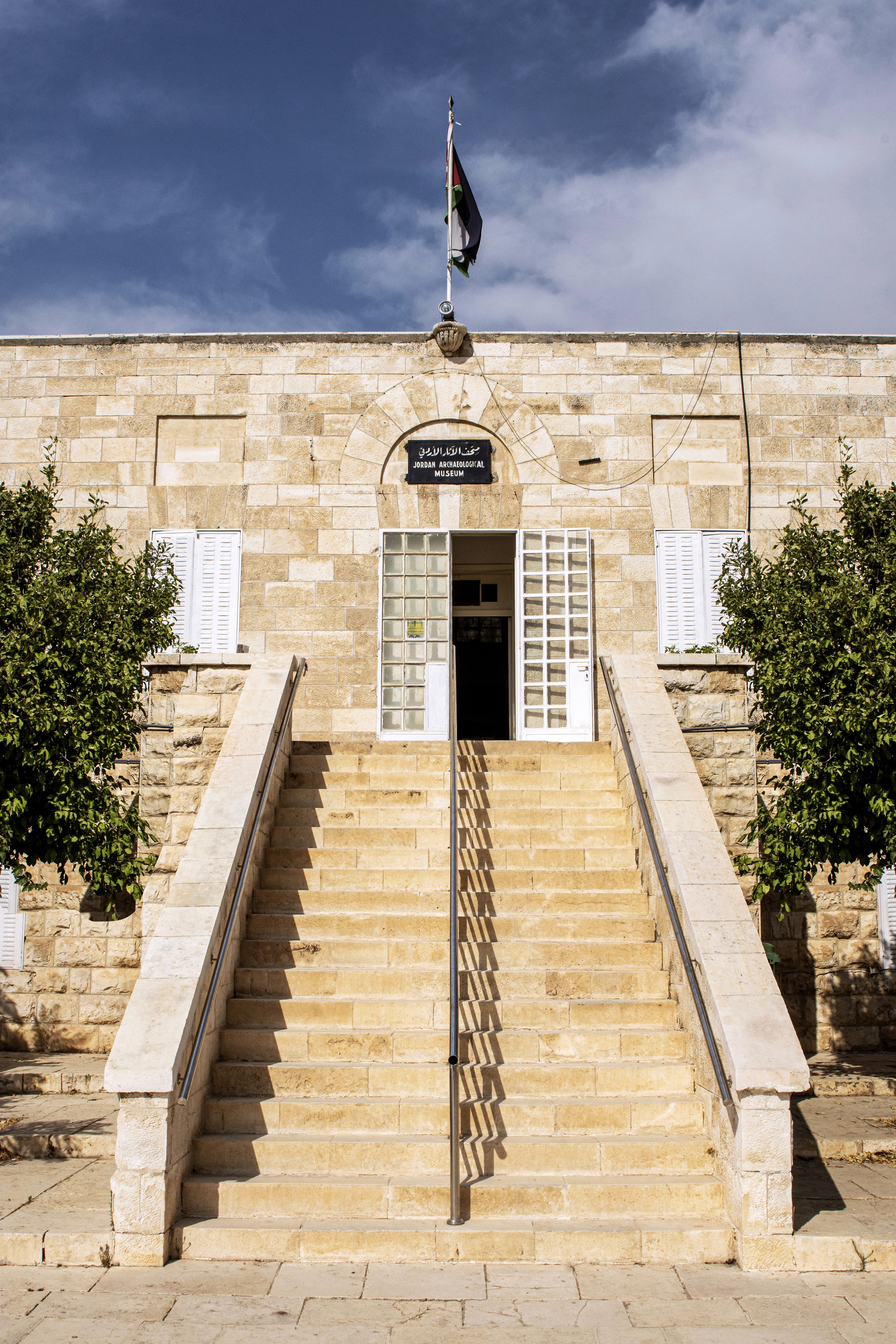 Stone steps rise to the Jordan Archaeological Museum's arched entrance atop Amman's Citadel hill under a clear blue sky.