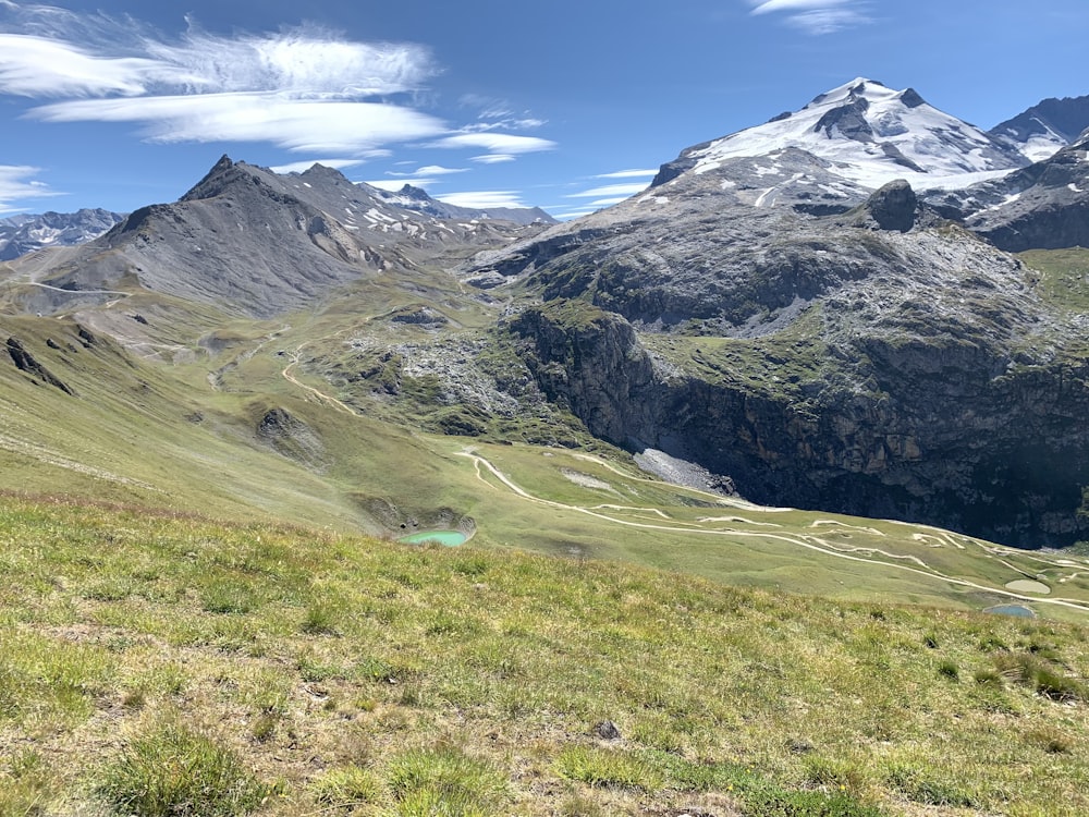 green grass field near snow covered mountain under blue sky during daytime